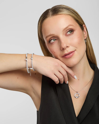 Woman wearing silver jewelry including a necklace, bracelet, and earrings on a plain background